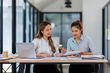 Asian Business women using calculator and laptop for doing math finance on an office desk, tax, report, accounting, statistics, and analytical research concept
