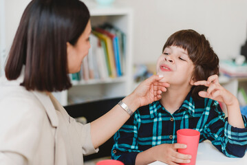 Woman speech therapist helps a boy correct the violation of his speech