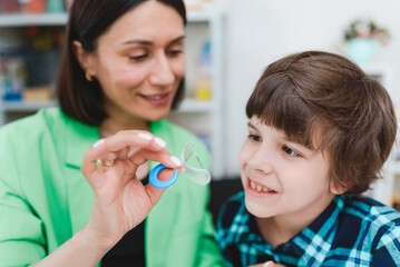 A female speech therapist shows a boy an orthodontic plate to correct his bite.