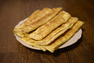 A close-up of traditional Ukrainian nalysnyky, thin pancakes or crepes, neatly rolled and arranged on a white plate. The golden-brown crepes are dusted with a light layer of cinnamon or sugar.
