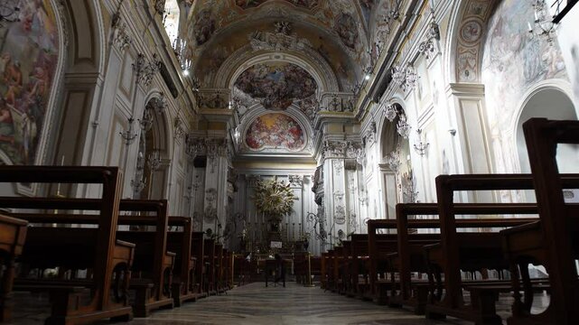 Low angle view walking past wooden pew chairs towards imposing altar in beautifully decorated San Benedetto church in Catania, Italy
