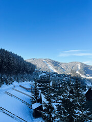Fototapeta premium Snowy mountain village surrounded by scenic forest and clear blue sky