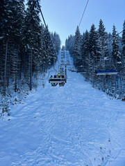 Chairlift ascending above a snow-covered forested ski slope during winter
