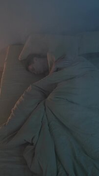 Man lying in bed coughing and struggling to breathe as smoke fills the room, indicating a dangerous house fire and life-threatening conditions. Vertical video