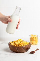 milk from a bottle pouring into a bowl with cornflakes, light background, breakfast