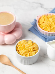 cornflakes in a bowl, milk and a cup of coffee on a light background, breakfast