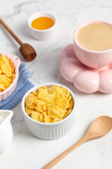 cornflakes in a bowl, milk and a cup of coffee on a light background, breakfast