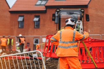 Construction workers utilizing surveying equipment on a building site in a residential area 