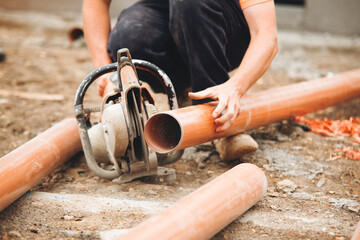 Construction worker uses saw to cut plastic pipes on a building site