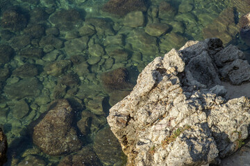 Macro Top view of Coastal rock formation in clear, calm blue-green water, with visible textured seabed and rugged, layered gray and beige rocks. Budva, Montenegro. High quality photo