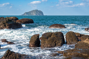 Gorgeous wave splashing on the rocks near the coastline, and Keelung island in the distance, in Keelung city, Taiwan.