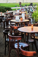 Outdoor cafe terrace with empty wooden tables and chairs. There are bicycles parked in the background.
