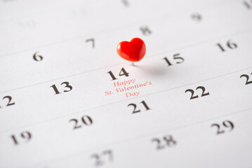 A small red heart-shaped pin marking Valentine's Day on a calendar page, symbolizing love