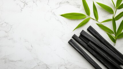 A composition of bamboo charcoal sticks with fine detailing, surrounded by fresh green leaves on a white background, representing sustainable natural resources