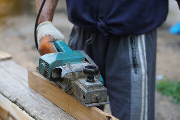 Closeup carpenter using electric planer with wooden plank in carpentry worksite. Concept, tool or...
