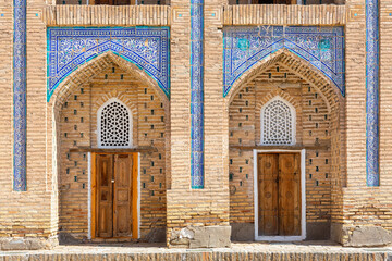 Close-up of madrasa cells, featuring ornate blue tilework, arched facades, wooden doors, and...