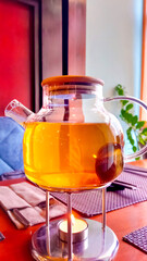 Glass teapot of herbal tea, with candle burning underneath, keeping it warm, on table in restaurant.