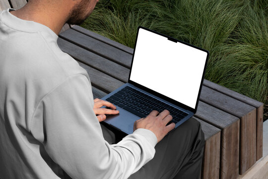 A person typing on a laptop computer mockup template in an urban outdoor park. Isolated surface to place your design. 