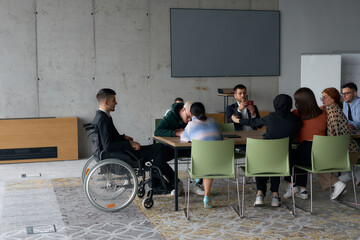 A diverse group of business professionals, including a man in a wheelchair, collaborate during a...