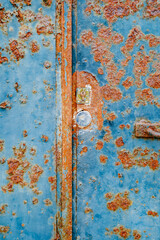 A close-up view of a heavily rusted blue metal door with significant patches of rust, highlighting the effects of weathering and oxidation over time. Ideal for industrial decay and corrosion