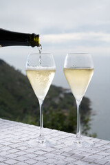 Pouring of cold sparkling wine, cava or champagne in two glasses on table with sea water view