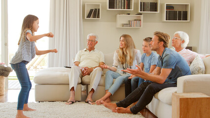 Multi Generation Family Sitting On Sofa At Home Playing Game Of Charades