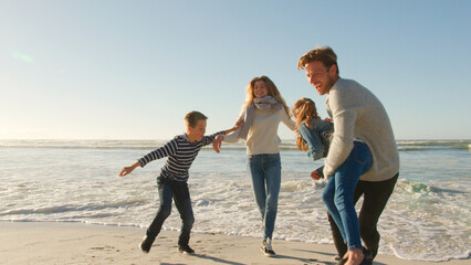 Family On Winter Beach Running Away From Advancing Waves