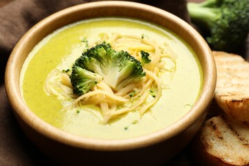 Delicious broccoli cream soup in bowl and croutons on table, closeup