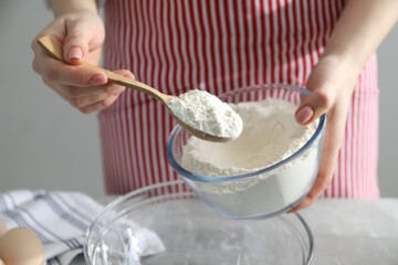 Making cinnamon rolls. Woman adding flour into bowl at gray marble table, closeup