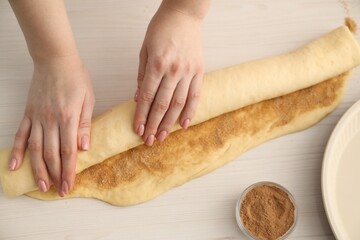 Making cinnamon rolls. Woman shaping dough at white wooden table, top view