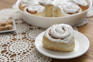Delicious frosted cinnamon roll on wooden table, closeup