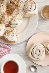 Delicious frosted cinnamon rolls and tea on light wooden table, flat lay