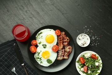 Tasty brunch. Delicious fried eggs, bacon, salad and glass of juice served on black table, flat lay. Space for text