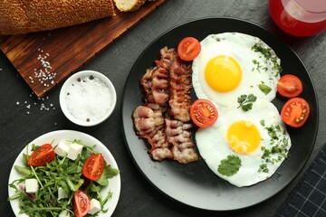 Tasty brunch. Delicious fried eggs, bacon, salad and glass of juice served on black table, flat lay