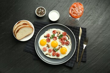 Tasty brunch. Delicious fried eggs with sausage and mushrooms served on black table, flat lay