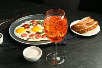 Tasty brunch. Aperol cocktail, delicious fried eggs with sausage served on black table, closeup