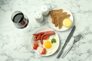 Tasty brunch. Fried egg, sausage, bacon and tomatoes served with wine on white marble table, flat lay