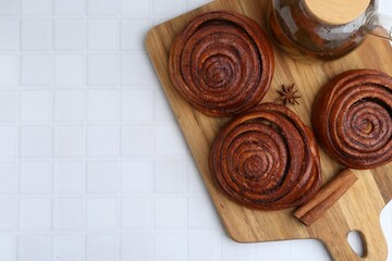 Delicious cinnamon rolls, tea and spices on white tiled table, top view. Space for text