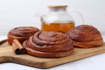 Delicious cinnamon rolls and stick on white tiled table, closeup