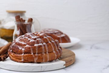 Tasty cinnamon roll with cream and spices on white marble table, closeup. Space for text