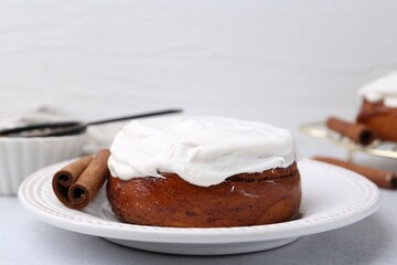Tasty cinnamon roll with cream and spices on light table, closeup