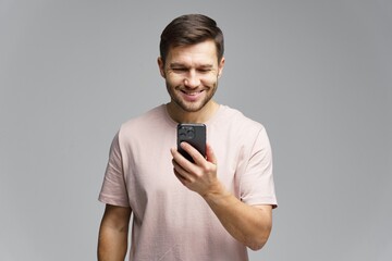 Man smiles while looking at smartphone screen in a bright studio background during daytime