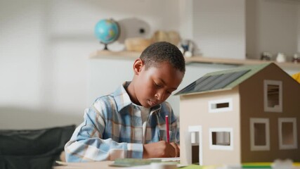 Close-up of young boy painting for school project. Framing highlights his attention to detail and precision, emphasizing craftsmanship required for building solar-powered house for science project