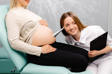 A gynecologist leans a stethoscope to a pregnant woman's belly and listens to the baby's heartbeat