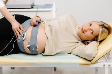Doctor prepares a pregnant woman for checking fetal heartbeat by fetal monitoring.