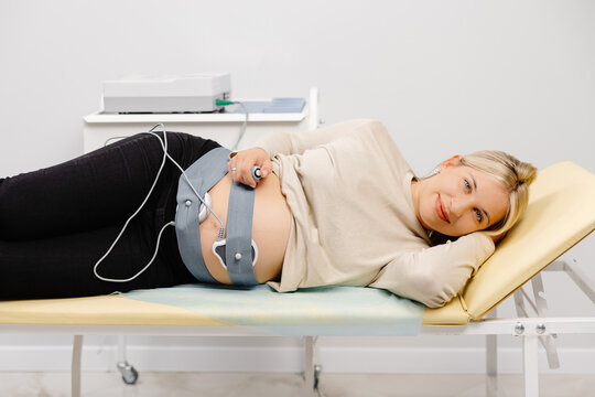 Woman pregnant checking fetal heart beat by fetal monitoring. Expectant mother with midwife adjusting sensors off cardiotocography