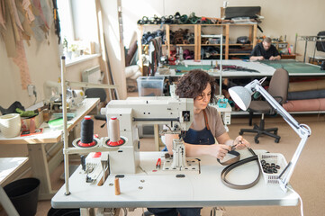 A woman tanner sews a leather belt on a sewing machine. 