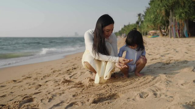 mother and toddler baby girl play with shell on the sea beach in Pattaya, Thailand
