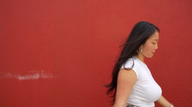 Full length frontal view of an asian young female urban dancer performing in the city dancing k-pop against a red wall