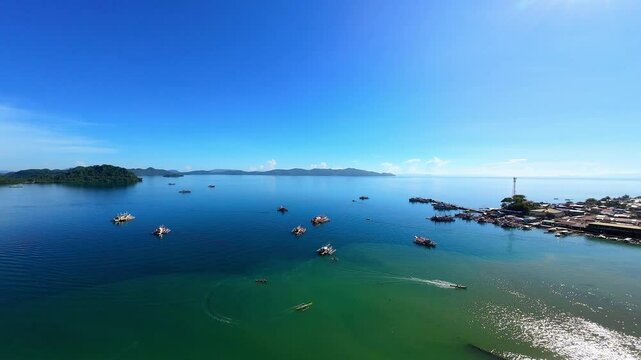 Static high-up aerial footage of Placer fishing port and town in Surigao Del Norte, Northern Mindanao, featuring colorful boats moored in a natural harbor under bright blue skies.